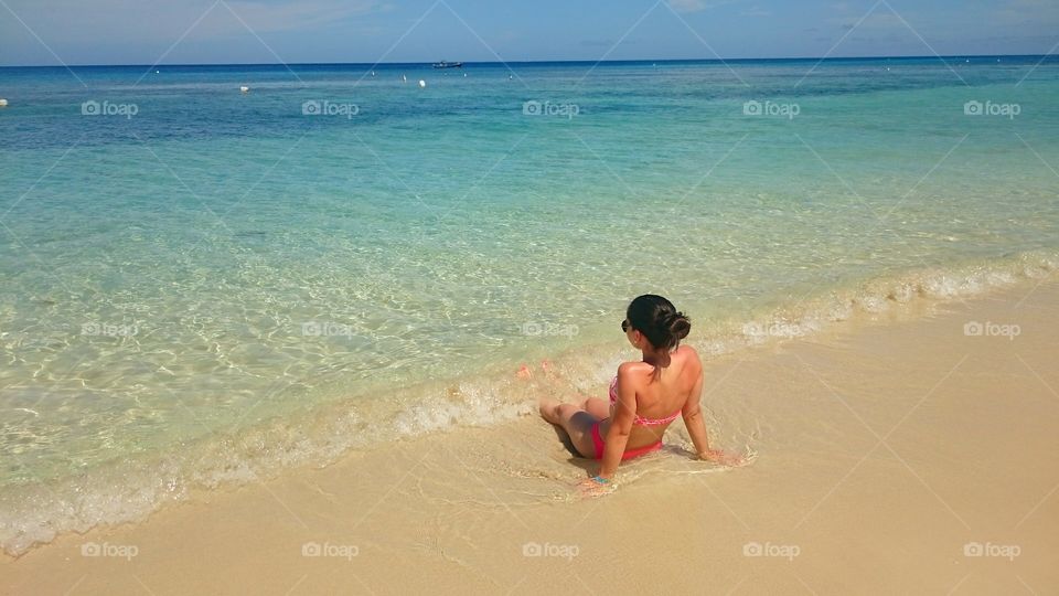 Relaxing. A young woman sunbathing at the shore of a beautiful white sand beach, clear water and the horizon in the background