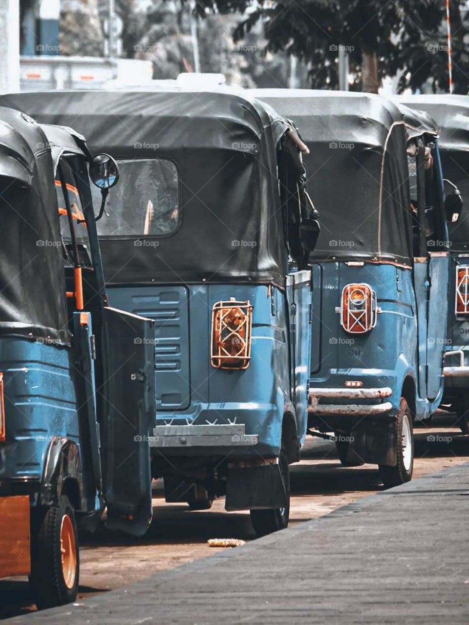 Portrait of several blue rickshaws parked in a row on the side of the road. Bajaj is a three-wheeled public vehicle that is popular in Indonesia