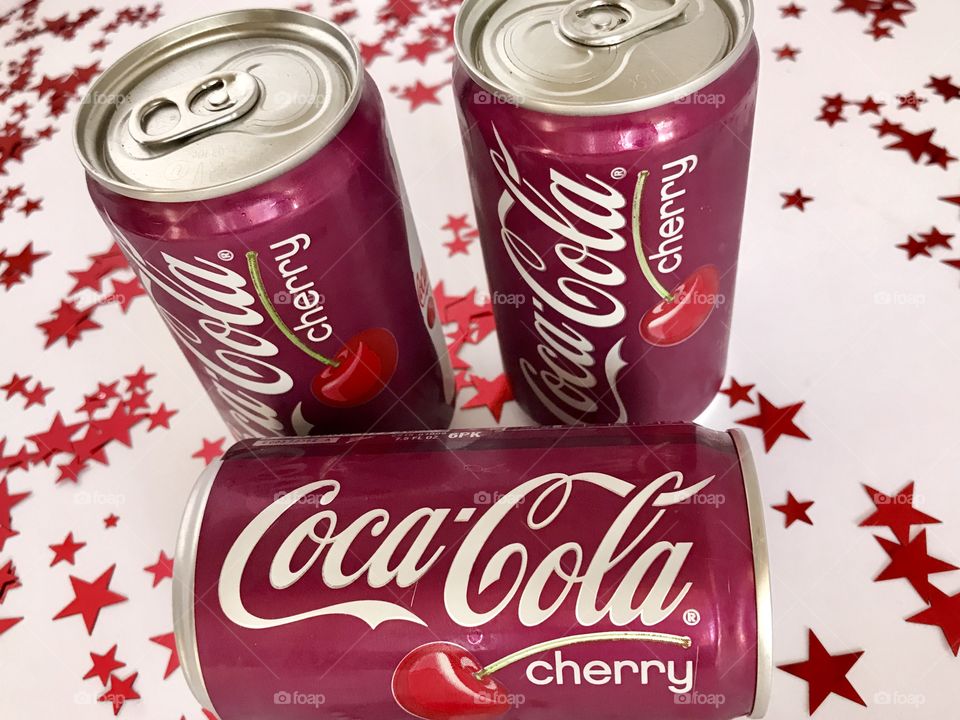Three cans of Cherry Coca-Cola on a white background with red stars