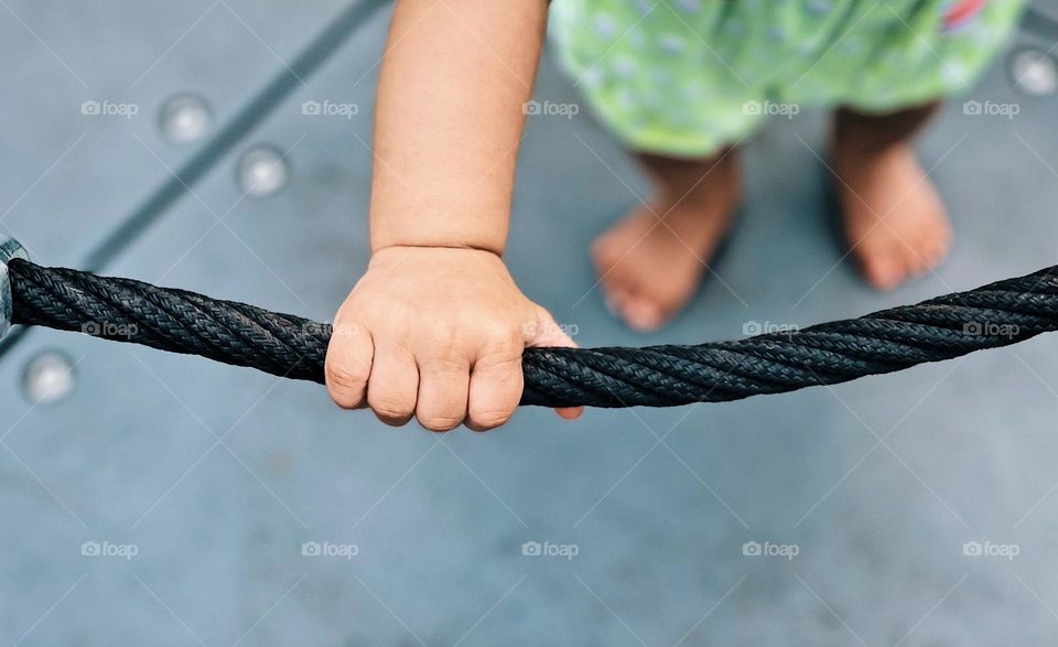 Baby holding onto rope handle for support, baby on the merry go round, baby at the park in the summertime 