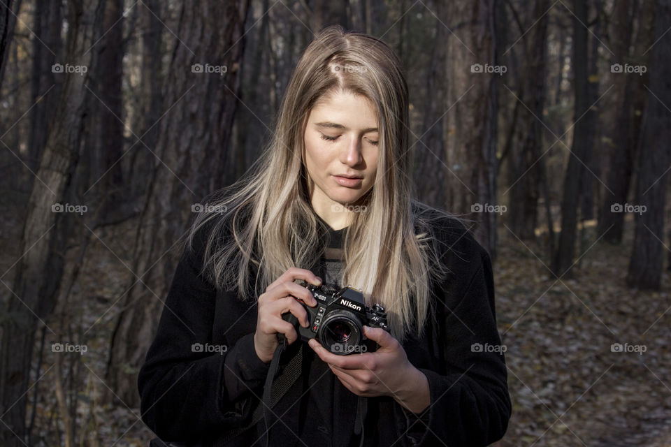 Beautiful blonde woman holding a camera in the forest