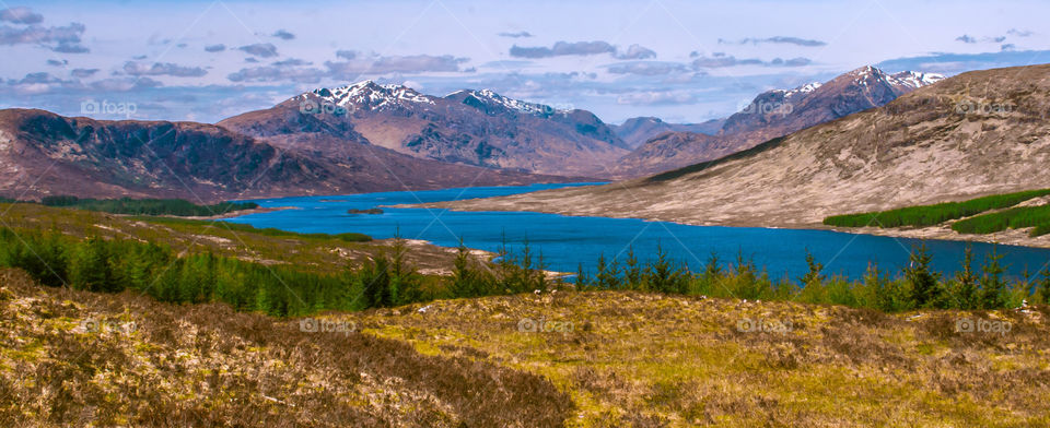 Tree lined hills and blue water lead to snow capped mountains in the Scottish Highlands - 2013