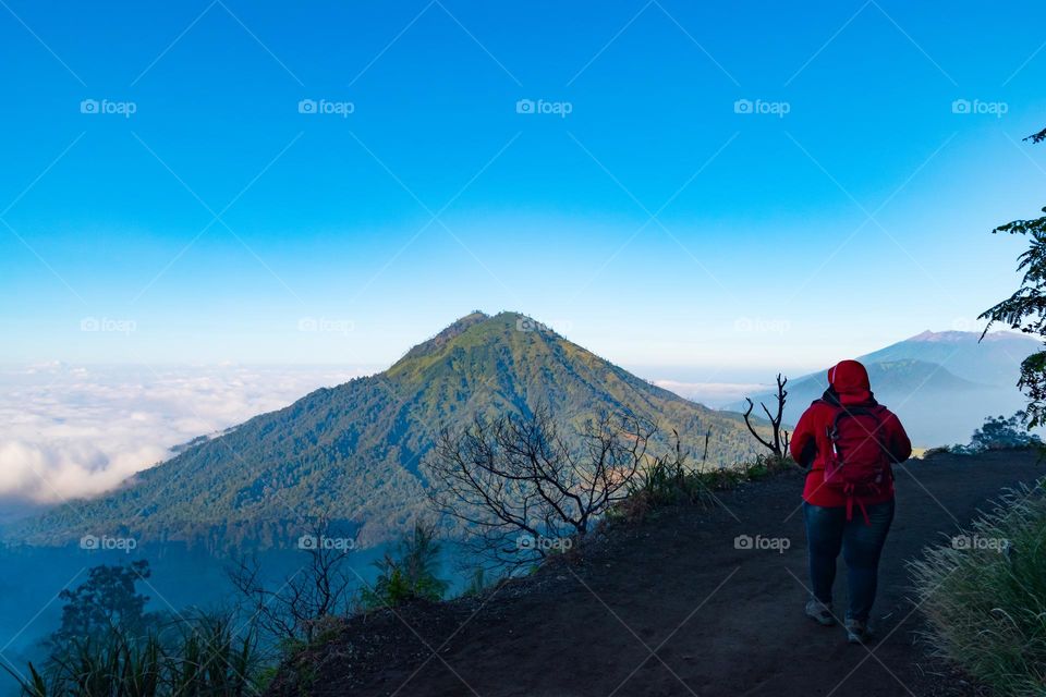 a person in red jacket walking along the side of a mountain with a view of another mountain in front of him/her with the clear blue sky, such a refreshment