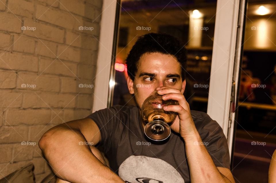 Man looking and drinking beer from a glass in bar at night 