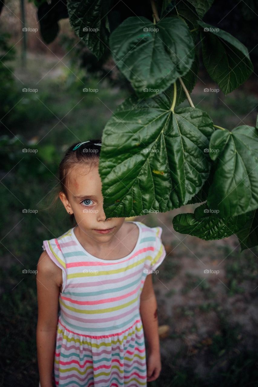 Summer Portrait of a Girl Hiding Behind a Large Leaf in the Garden