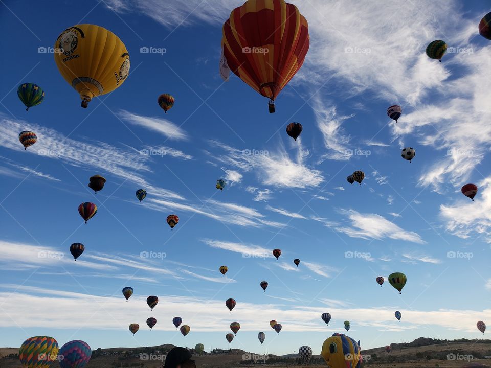 Silhouettes of hot air balloons against a bright blue sky with white clouds