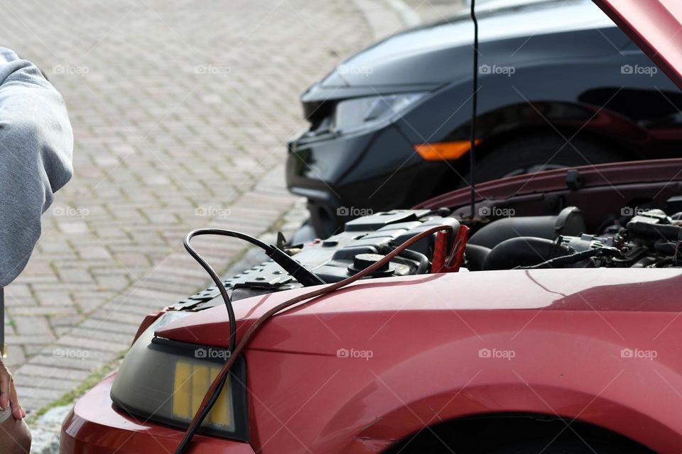 An older gentleman connects jumper cables to his Ford Mustang as he awaits a jump start from a fellow neighbor.