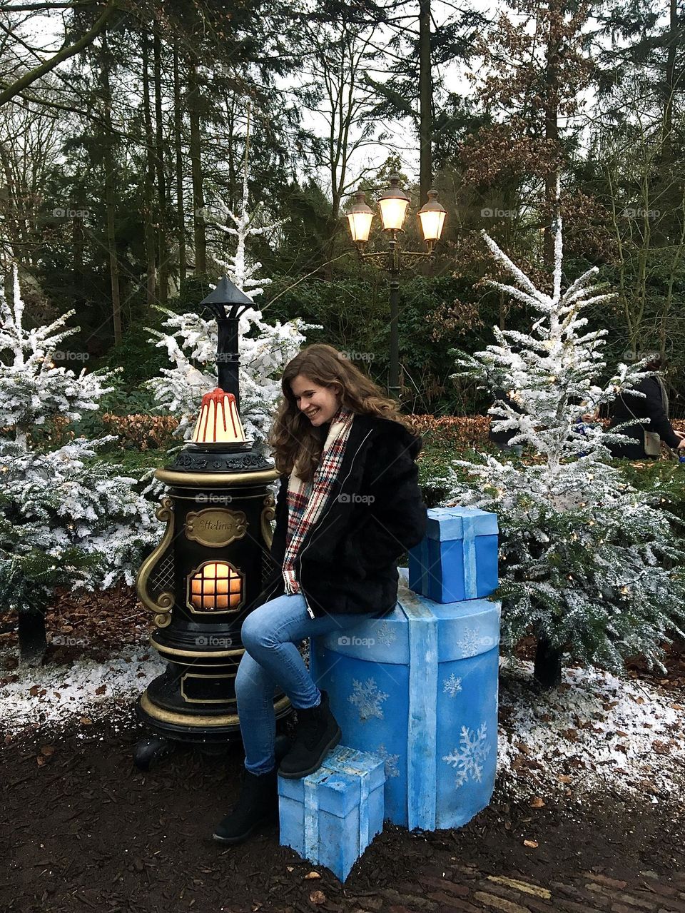 Girl sitting on gift boxes in front of Christmas trees