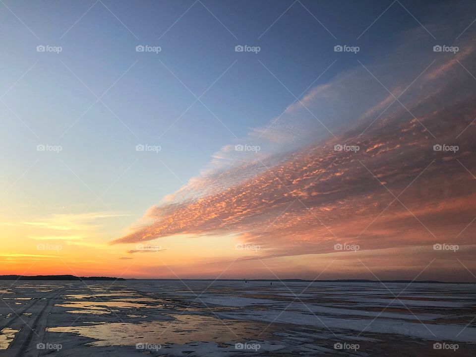 Orange wispy Clouds over a snow covered frozen lake 