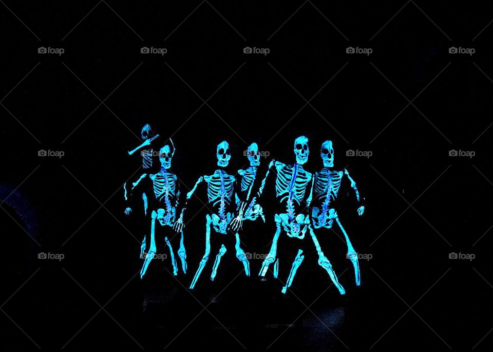 performance from group of fun and entertaining glowing skeletons dancing in a black room for Halloween