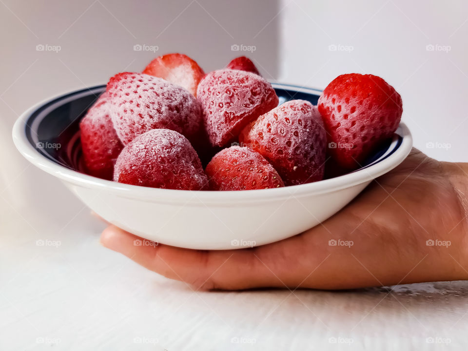 Holding a bowl of delicious frozen strawberries.