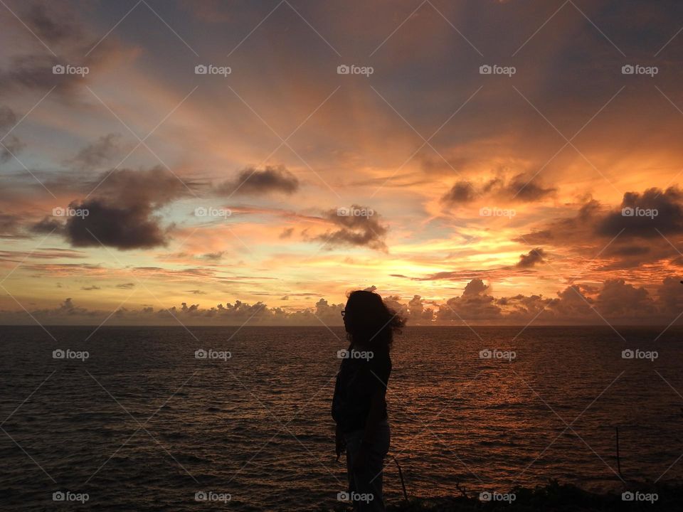 a woman is standing on the edge of a cliff looking at the sunset 🍃🌞🌥