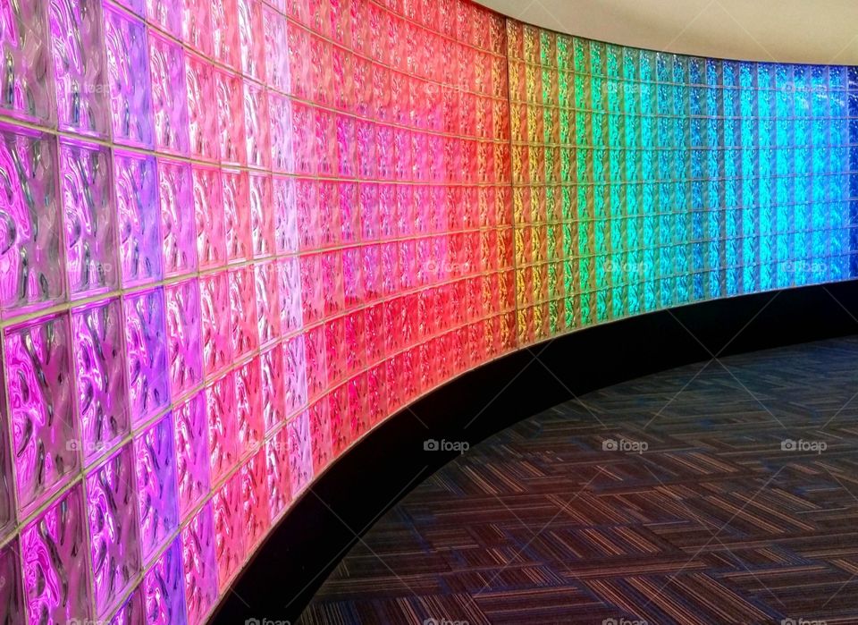Curved lit up rainbow colored glass wall inside airport