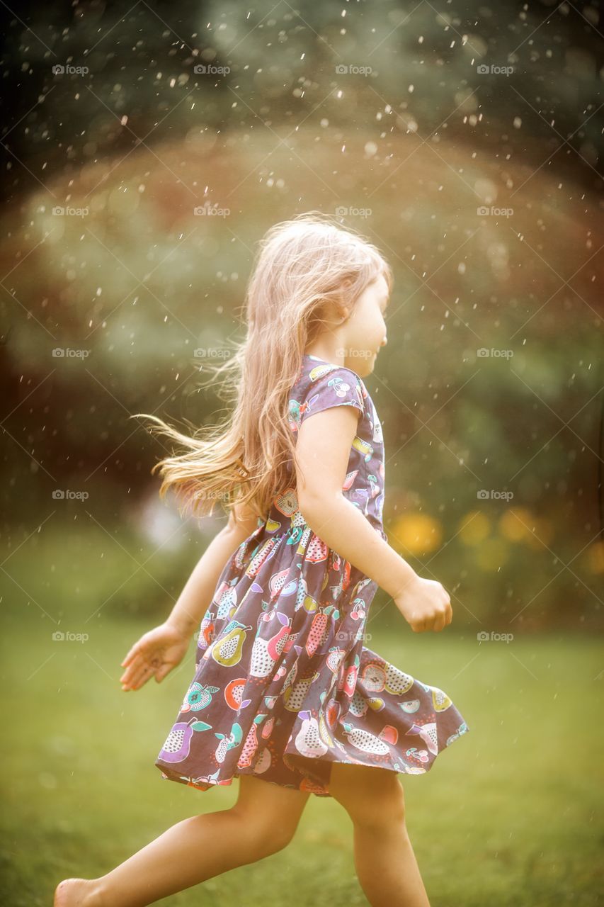 Little girl running under rain in sunlight