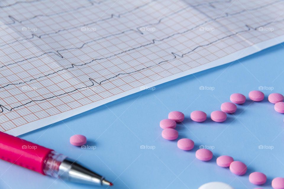 Pills and medicines lie on a blue background with an electrocardiogram of the heart.
