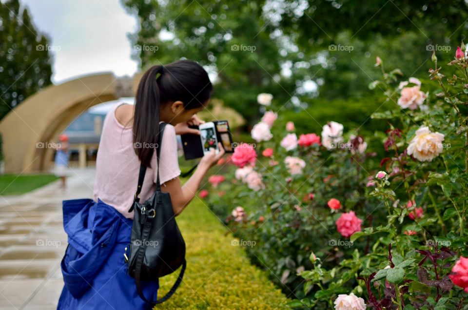 Girl in pink taking pictures of pink flowers in a beautiful public garden.