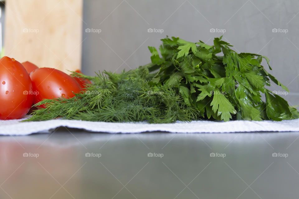 Fresh, bright, juicy vegetables and herbs for preparing salads and other vegetable dishes are on a gray, kitchen worktop.