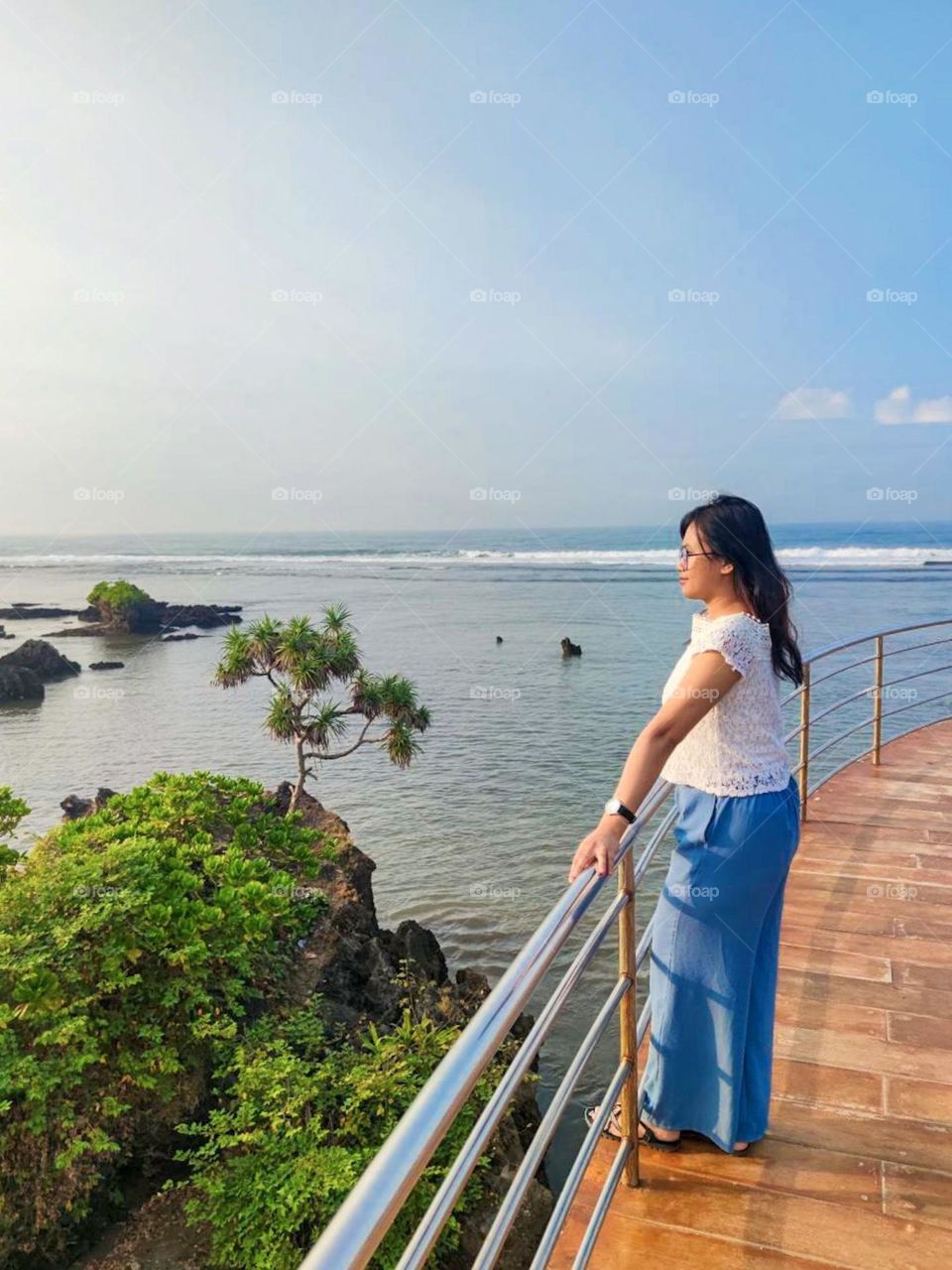 Portrait of a young woman standing on the railing looking at the beautiful sea view with a clear sky