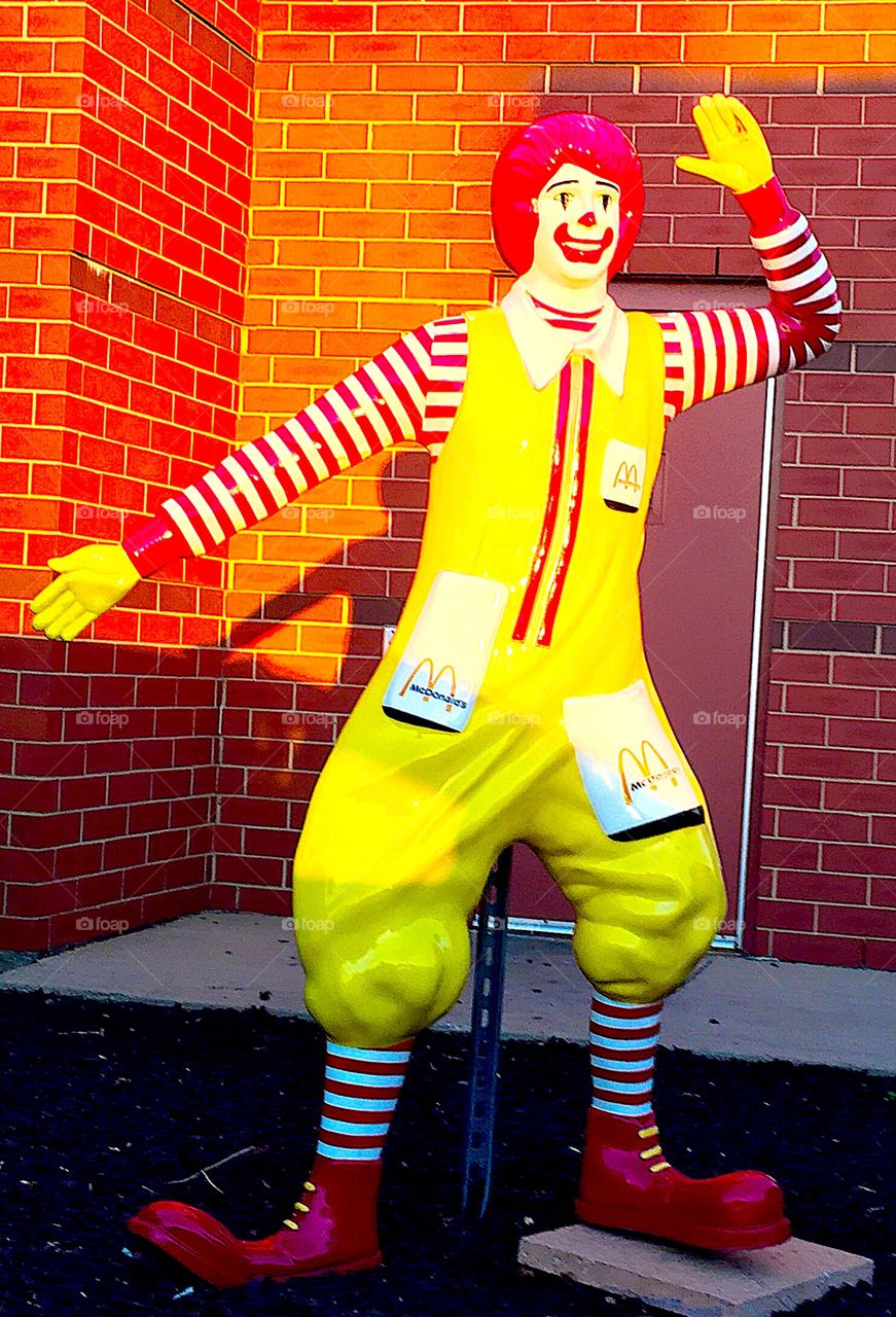 McDonald’s bright yellow and red, standing, waving, Ronald McDonald statue outdoors on bright sunny autumn day