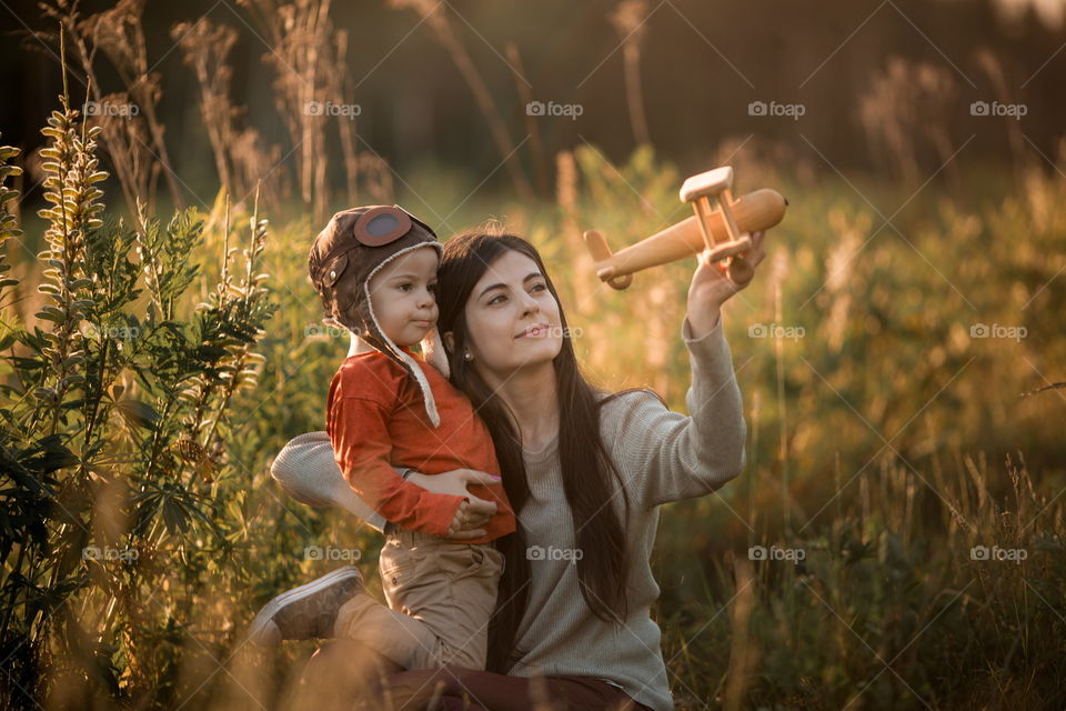 Mother with son playing with wooden plane at sunset