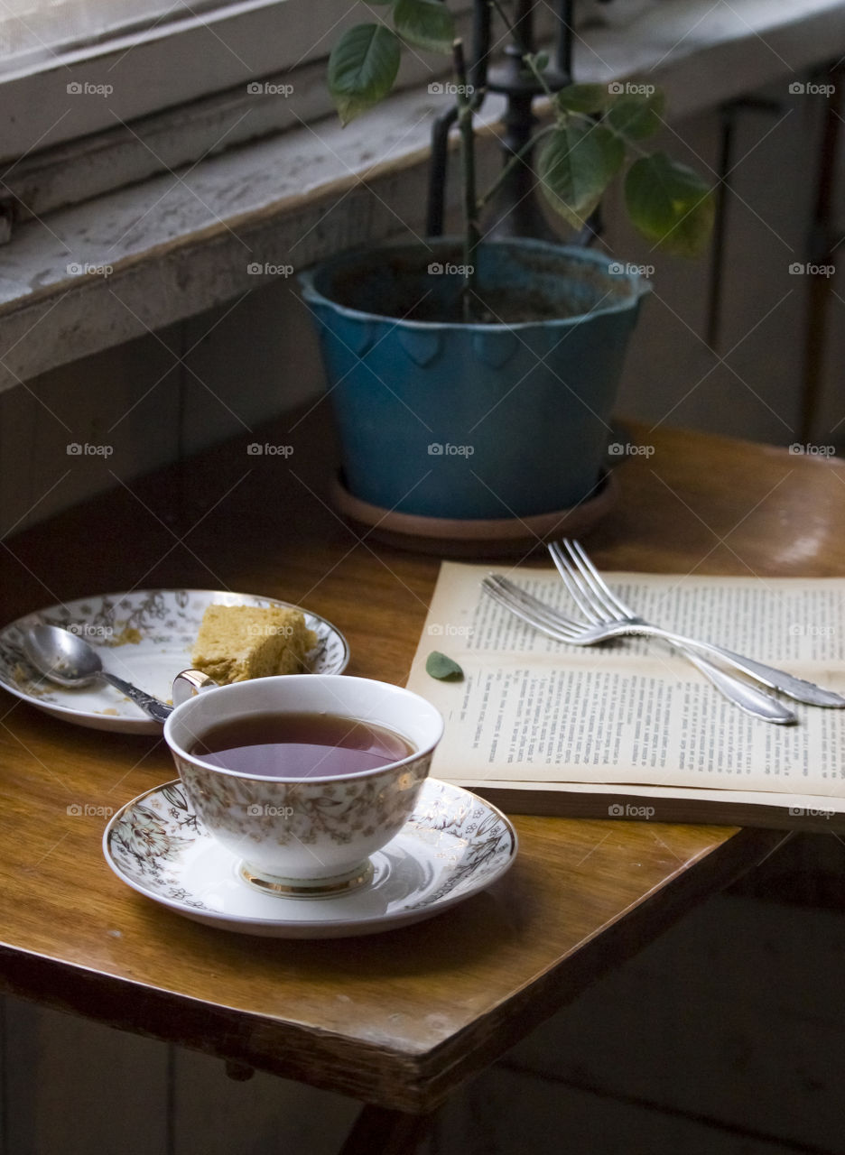 a cup of tea book, cake and home plant on the table