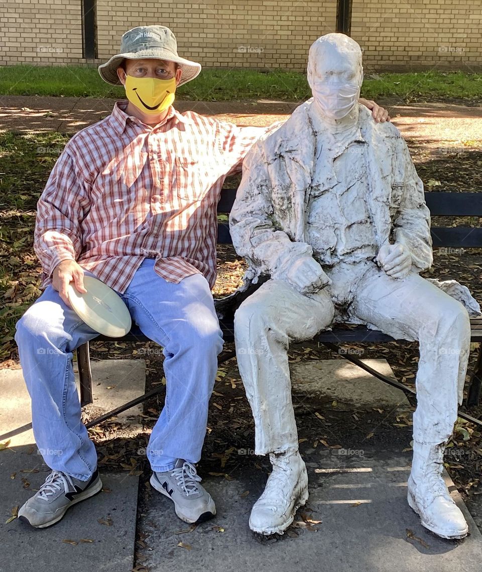 Masks on statue and man sitting together 