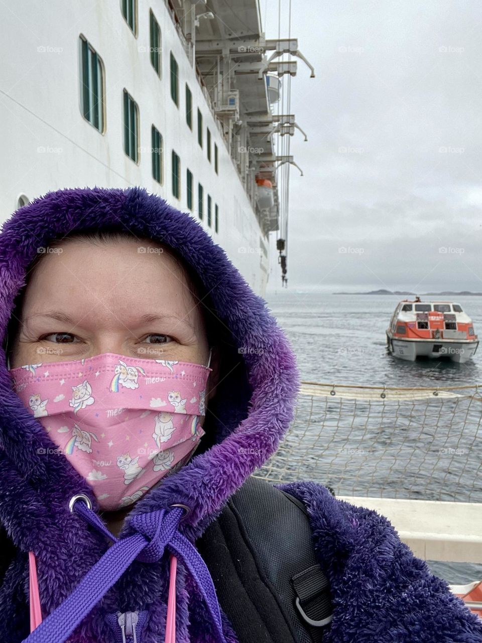 A person on a cold day with a cruise ship and a tender boat in the background