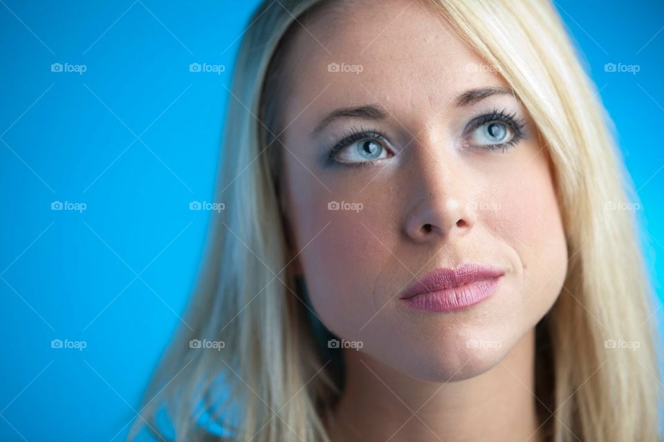 Close up portrait of girl  with blonde hair and blue eyes gazing up and off to the side on a blue background 