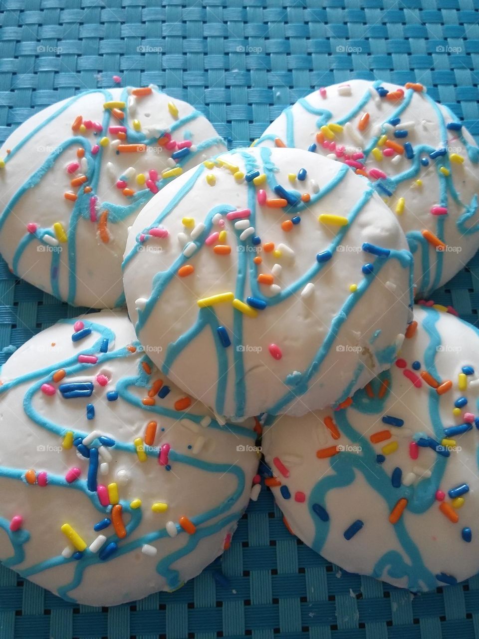 In this photo there are 5 medium sized sugar cookies with icing and sprinkles on top.