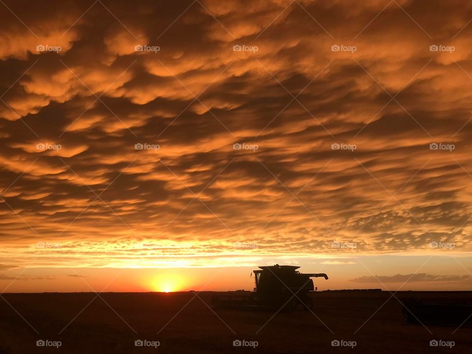 Orange sunset sinking down behind John Deere tractor