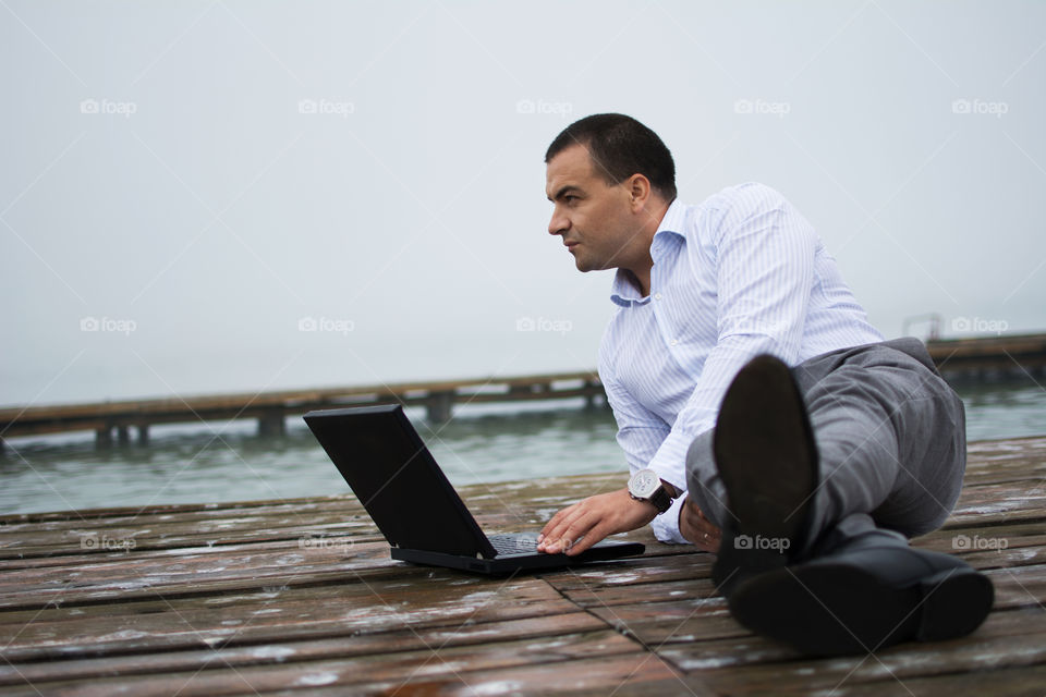 Man on lake dock with laptop