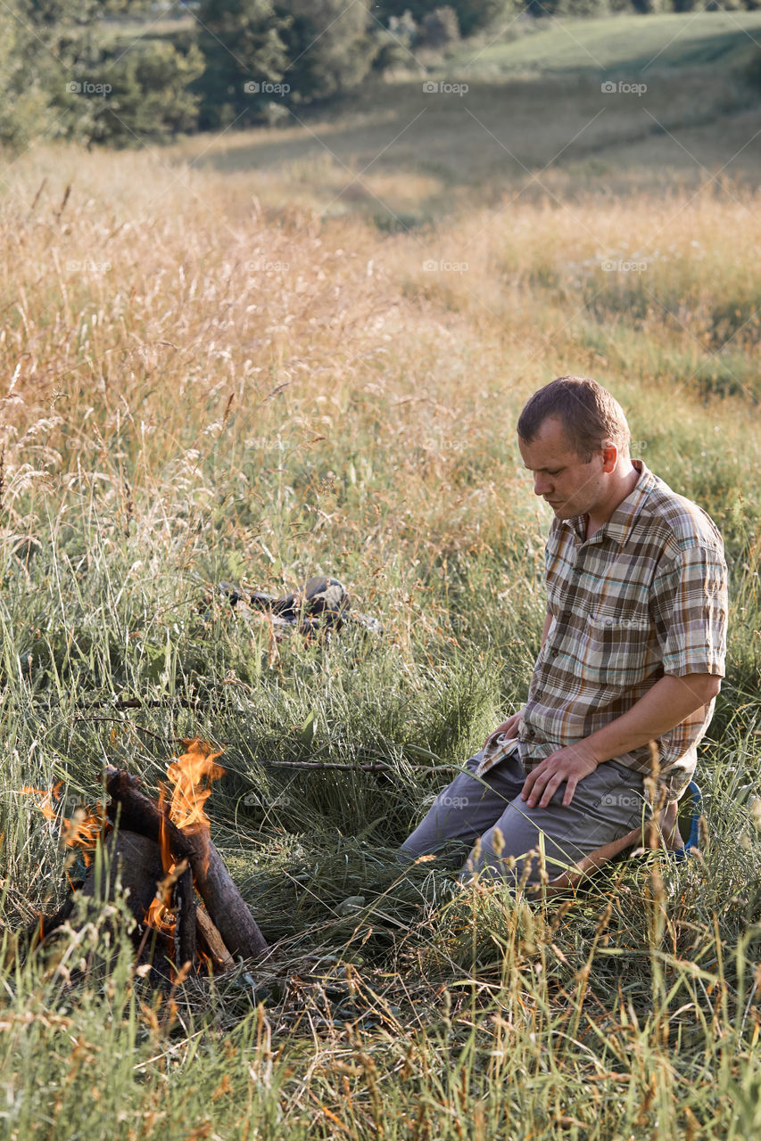 Man starting a campfire, blowing on a fire. Little girl sitting in a grass beside a campfire. Candid people, real moments, authentic situations