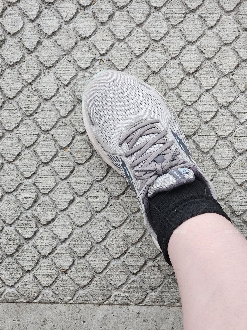 leg wearing sock and shoe walking on patterned cement