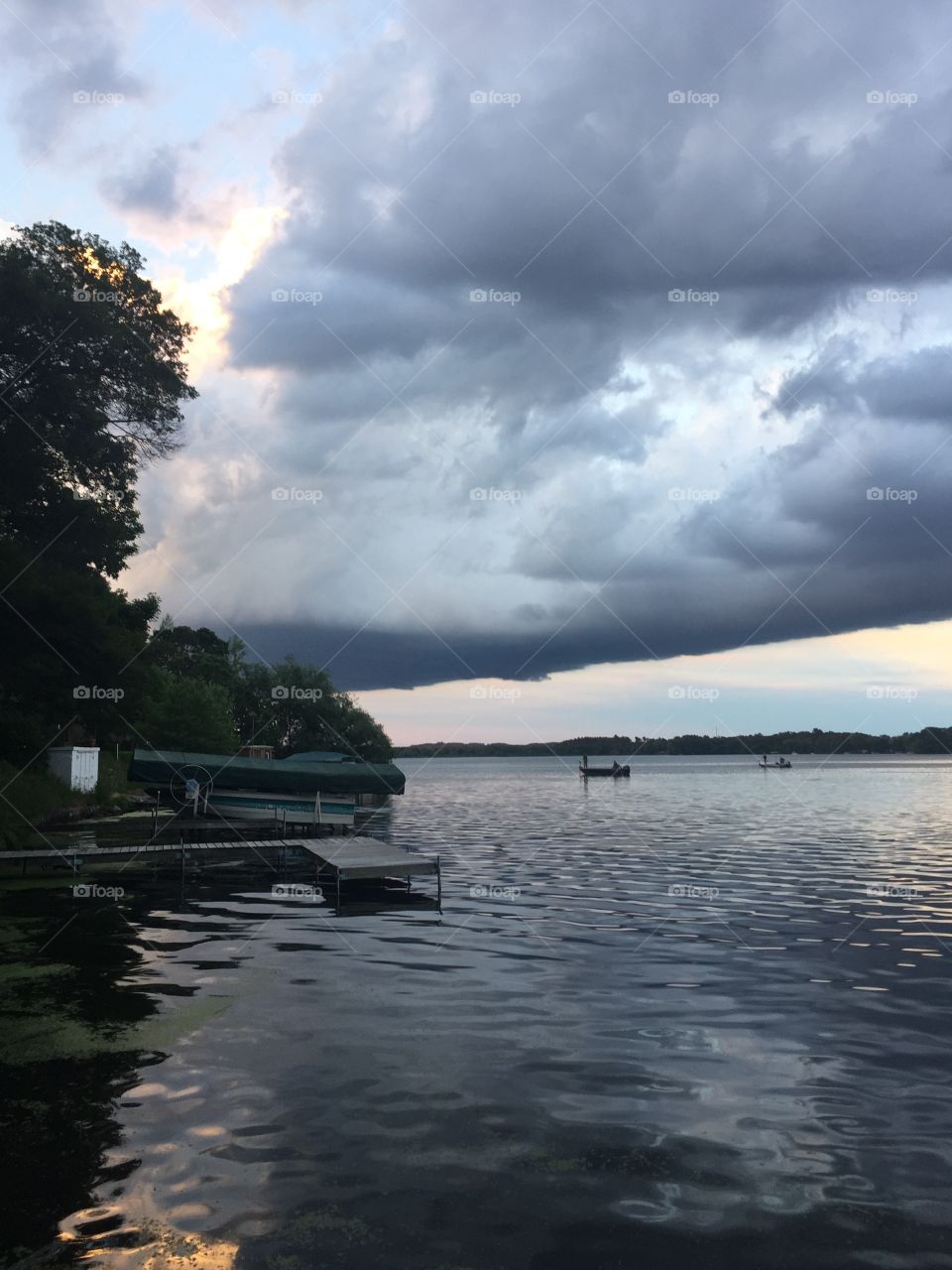 A looming storm cloud splits the sky over the lake. A few straggling boats hurrying back to shore before the storm hits.