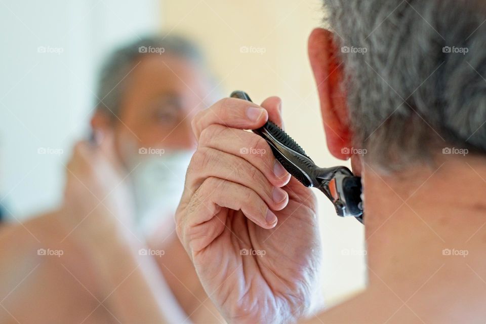 Man shaving looking at his reflection on a mirror