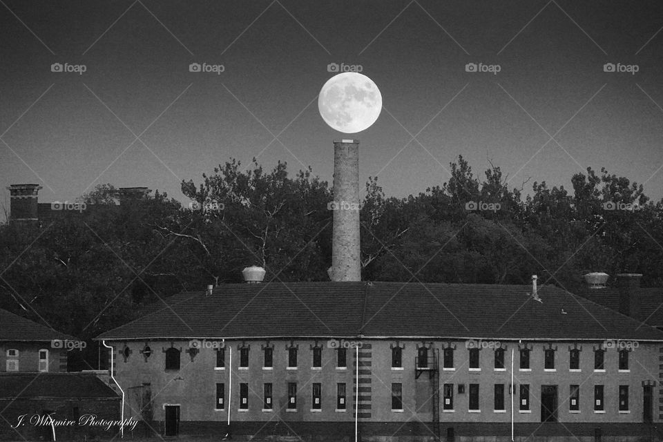A full moon rises above a smokestack on one of the buildings that makes up the Ellis Island museum