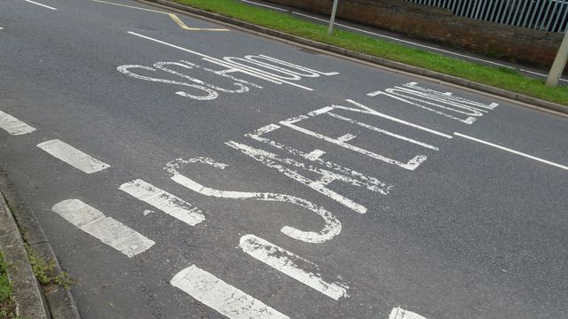 Road signs , painted road sign stating in English : school safety zone . 
road safety. road markings