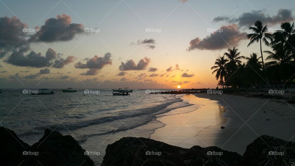 sunset at the island of Barbados in the Carribean sea with palm tree and boat silhouettes and clouds in a blue and orange sky