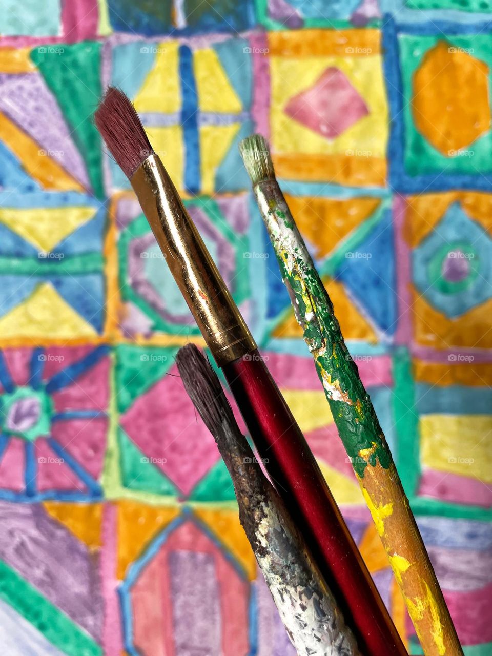 Close-up of three brushes of paint over a colorful watercolor painting