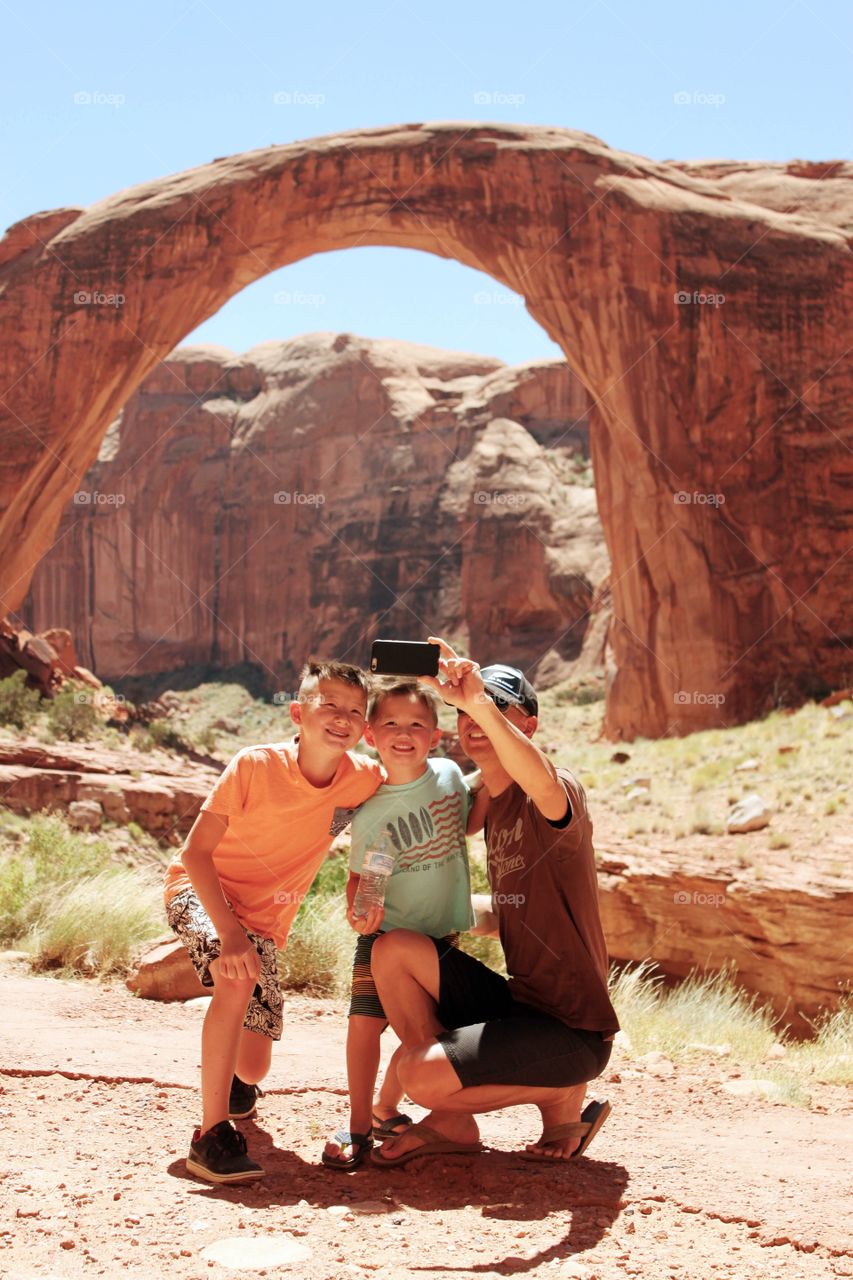 Father with his children taking selfie in front of Rainbow Bridge, Utah