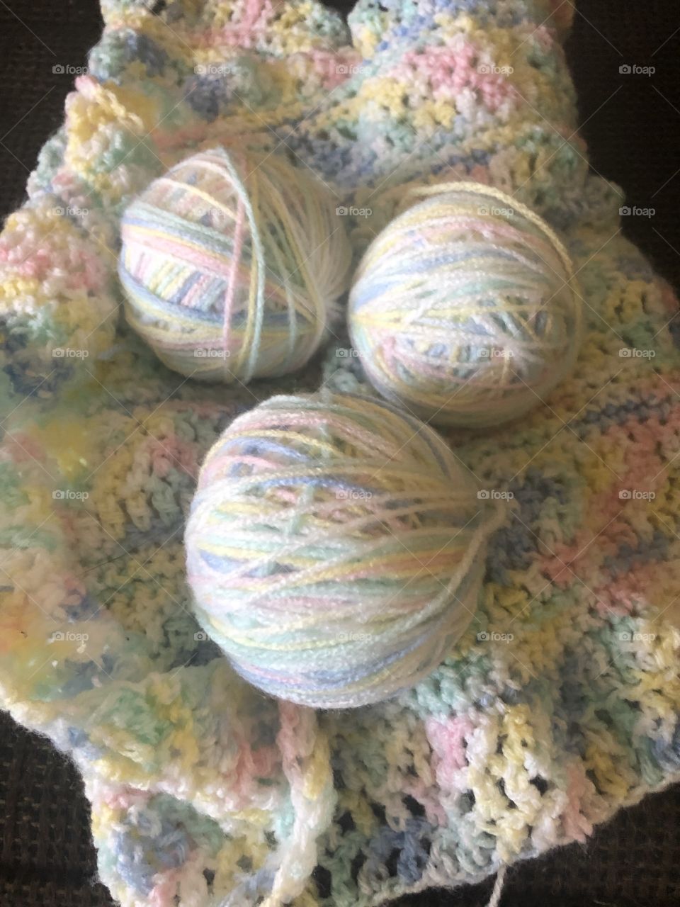 Balls of yarn on top of a baby Afghan. 
