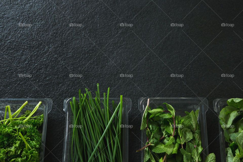 Various freshly picked green leafy herbs in a recyclable plastic boxes on a black background