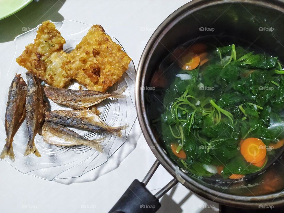 A pot of clear spinach soup with sliced ​​carrots and a side dish of fried salted fish and fried tempeh. One of Indonesia's simple home cooking menus