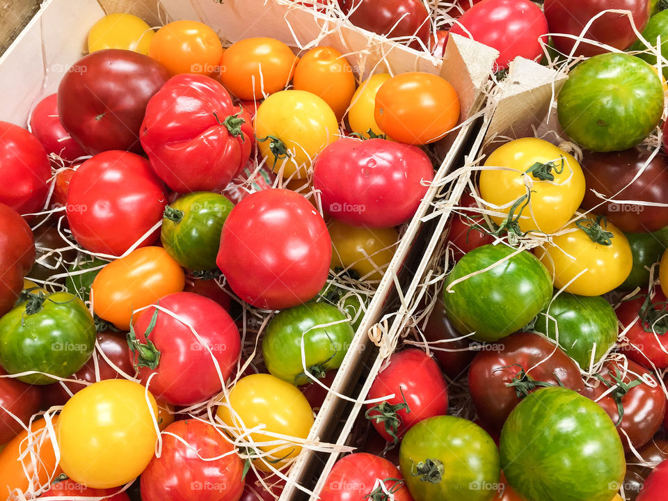 Fresh organic cultured tomatoes in different colors and flavors laying in wooden boxes for sale at farmers market