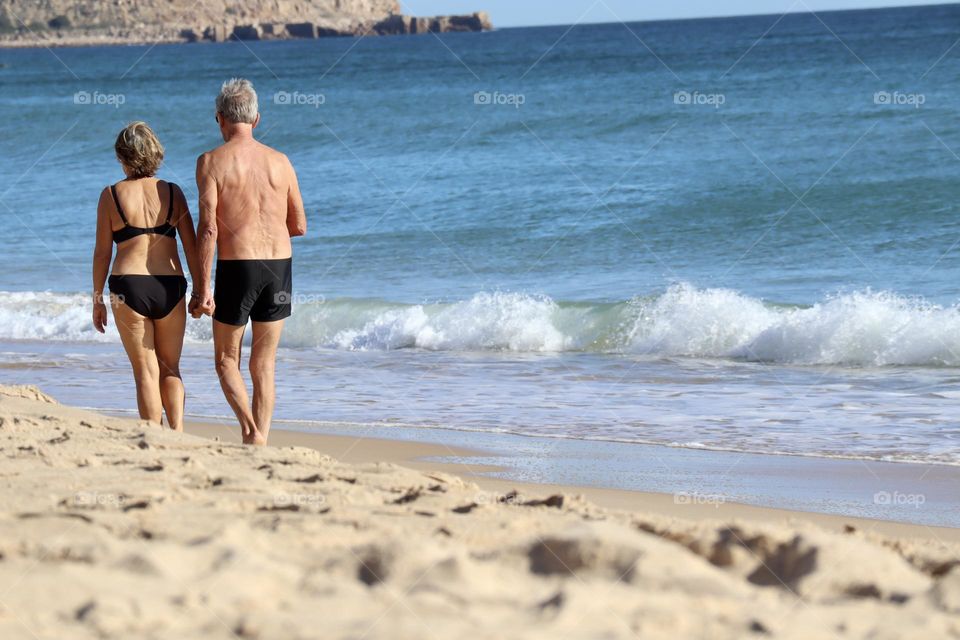 Old couple walking on the beach holding hands