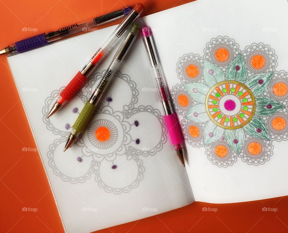 A kids coloring book. The picture shows some flowers painted and four color pen on it. Orange background. 