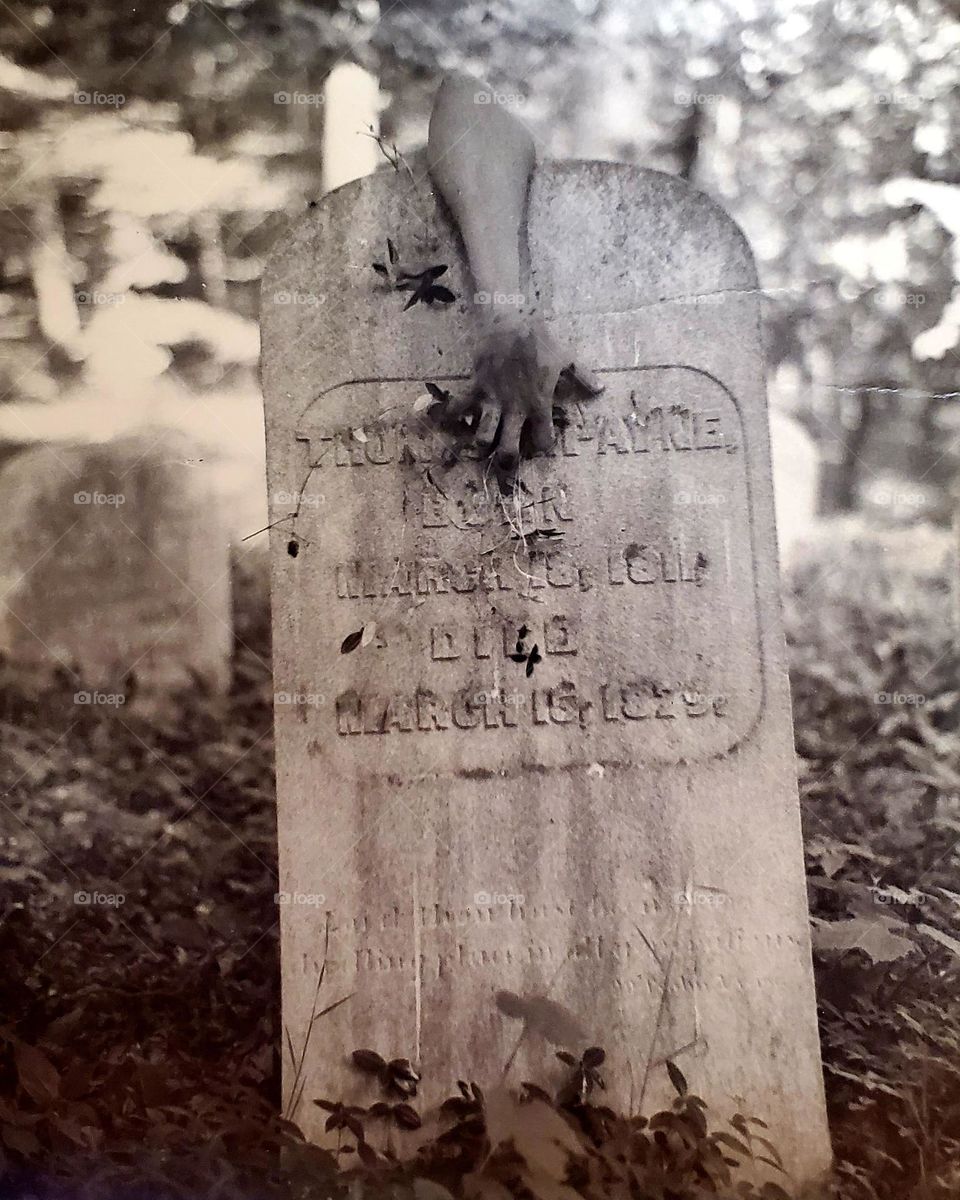 sepia-toned photo of old tombstone with a disembodied arm draped over the top
