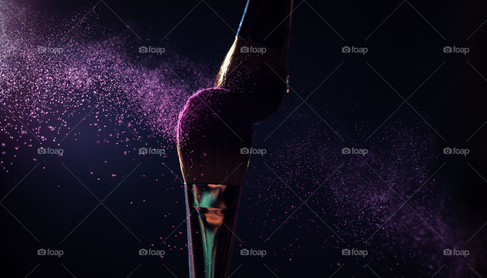 Art of visage. Closeup photo of two professional black make-up brushes with purple powder isolated on black background with copy place.