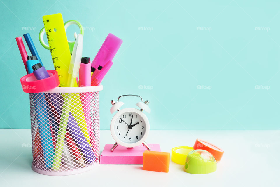 bright colored stationery in a glass and next to it and a white small alarm clock