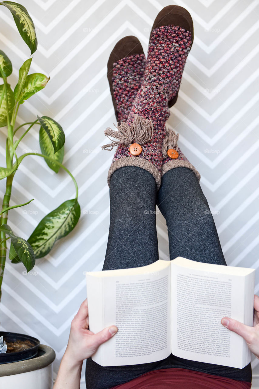 Woman laying on the floor while reading a book with legs propped up against the wall